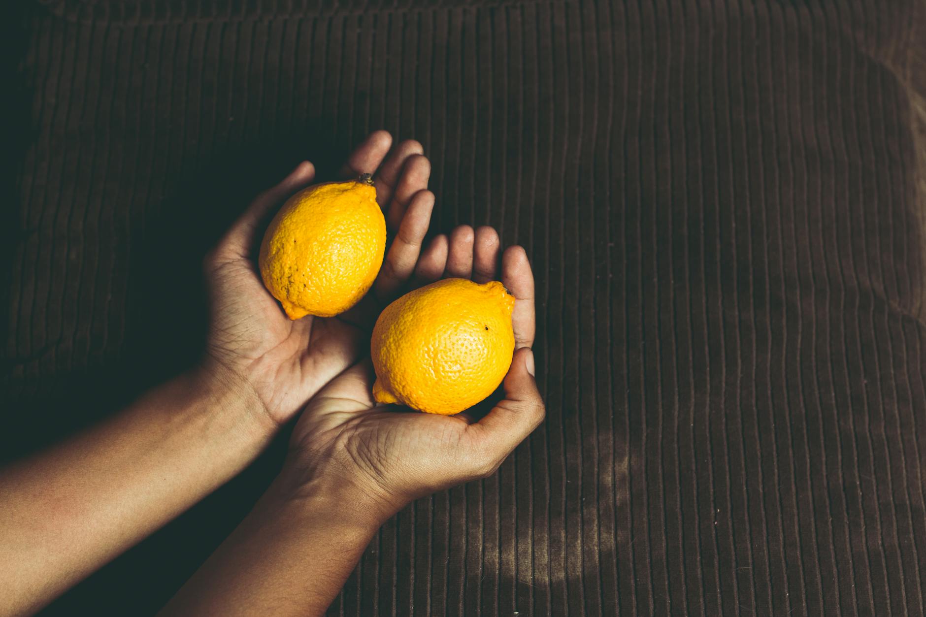 Dos limones frescos en las manos sobre fondo marrón, simbolizando frescura y renovación del deseo