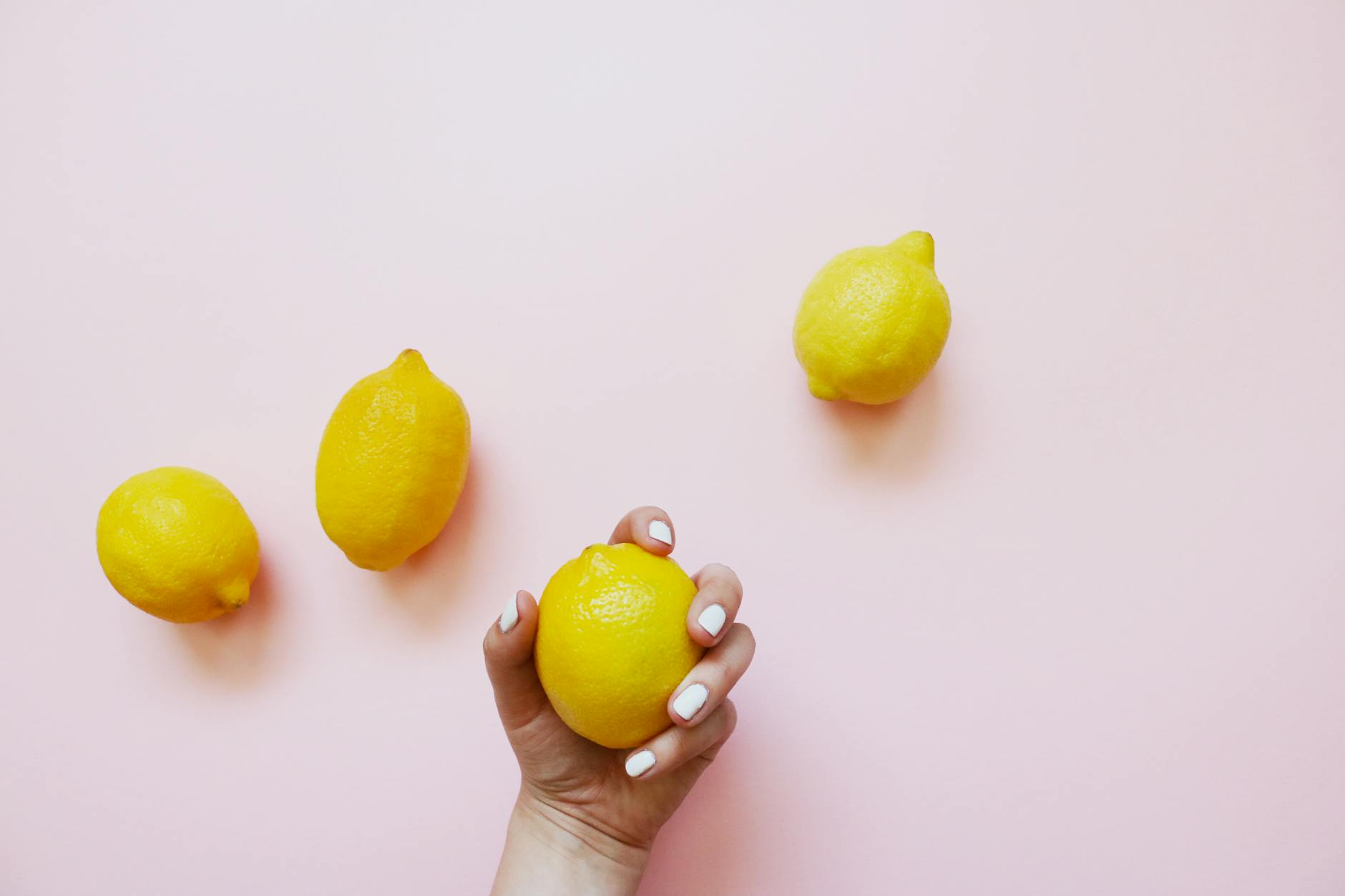 Woman holding fresh lemon on soft pink background surrounded by additional lemons