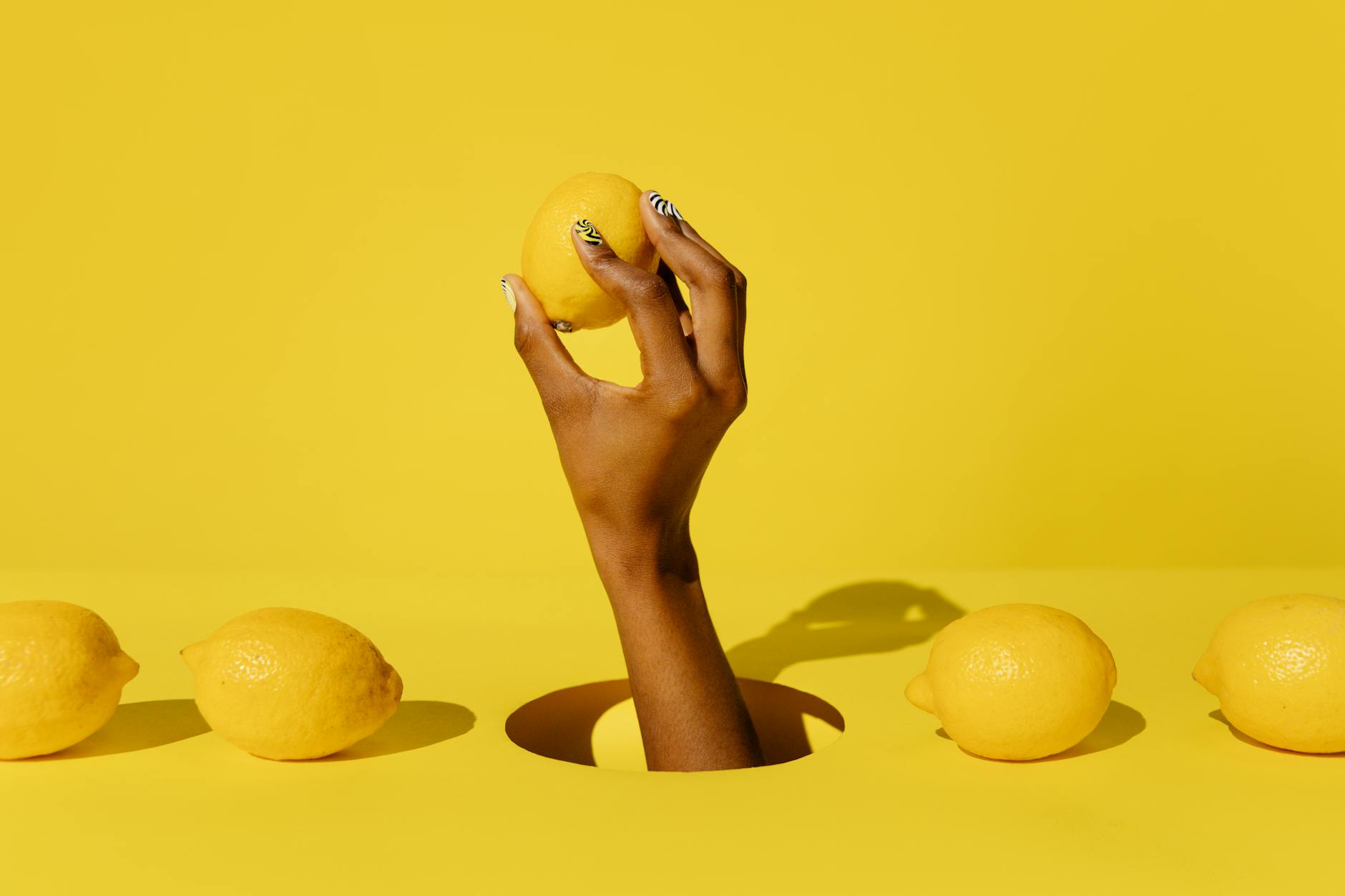 Mano sosteniendo un limón fresco contra un fondo amarillo vibrante