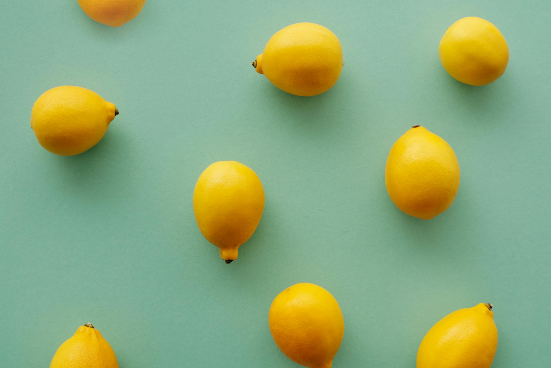Limones brillantes amarillos colocados sobre fondo verde pastel, creando una composición fresca y vibrante.