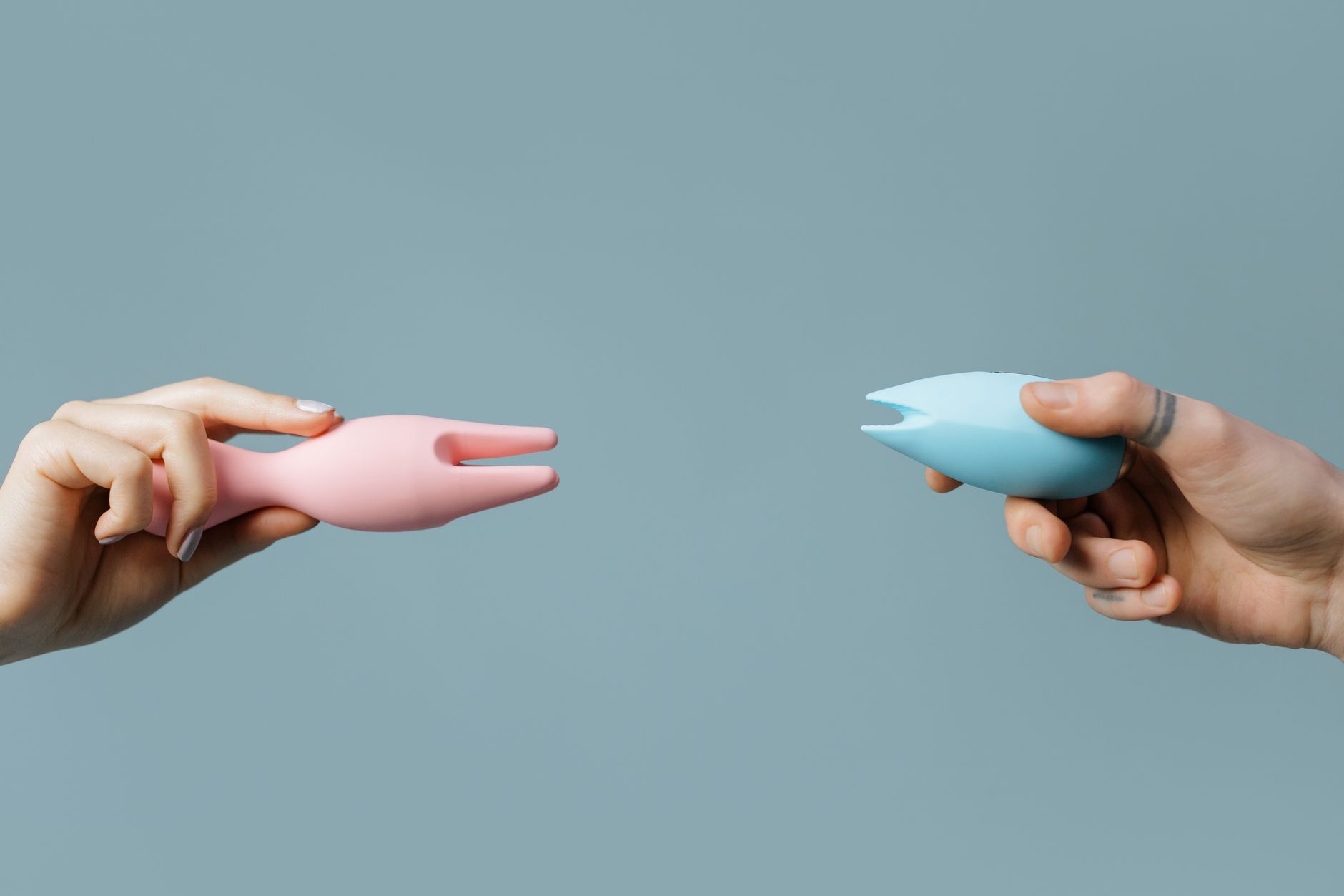 Woman with eyeglasses holding blue and pink silicone vibrators in a contemplative manner
