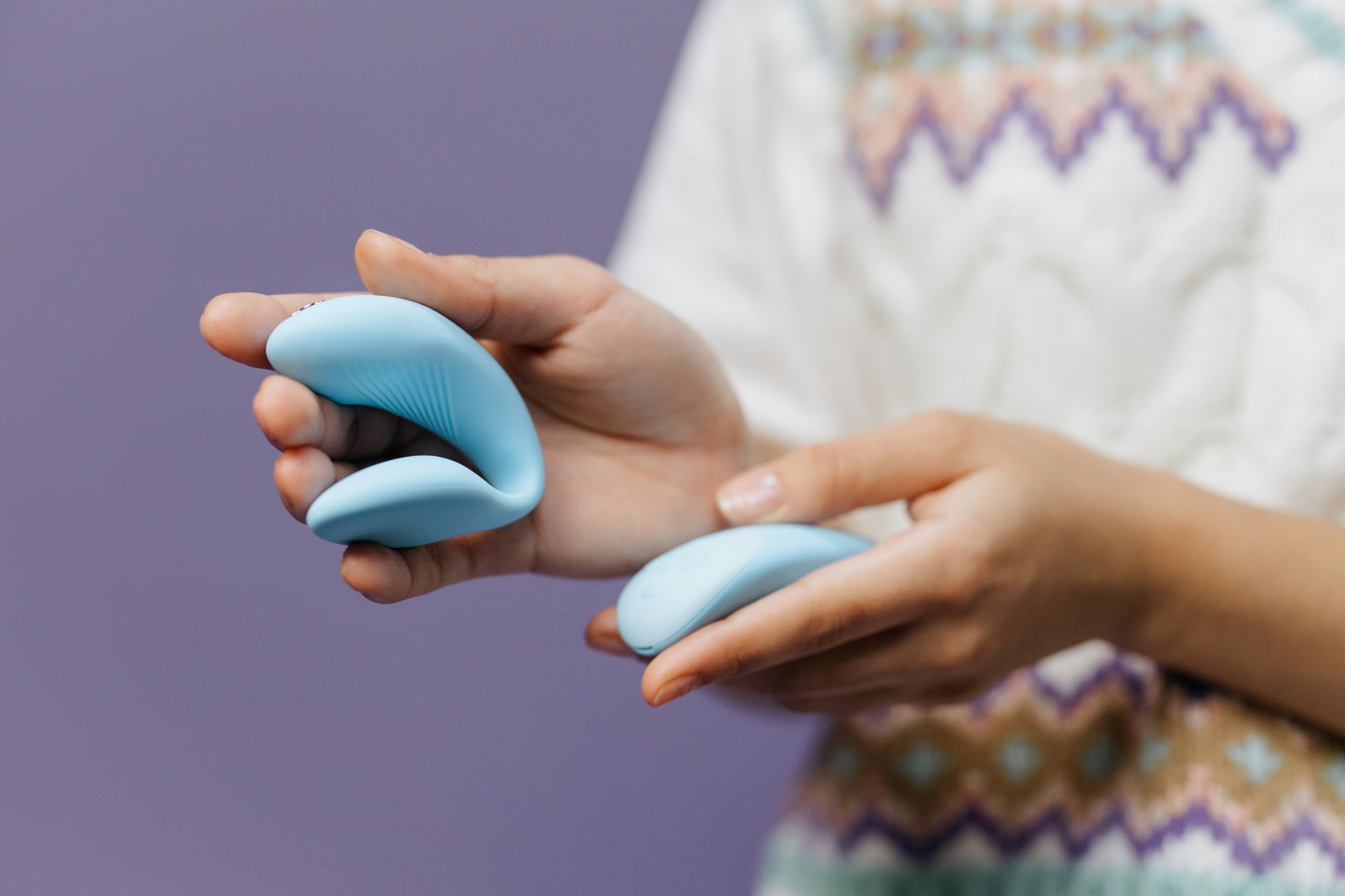 Primer plano íntimo de manos sosteniendo un vibrador azul elegante contra un fondo púrpura.