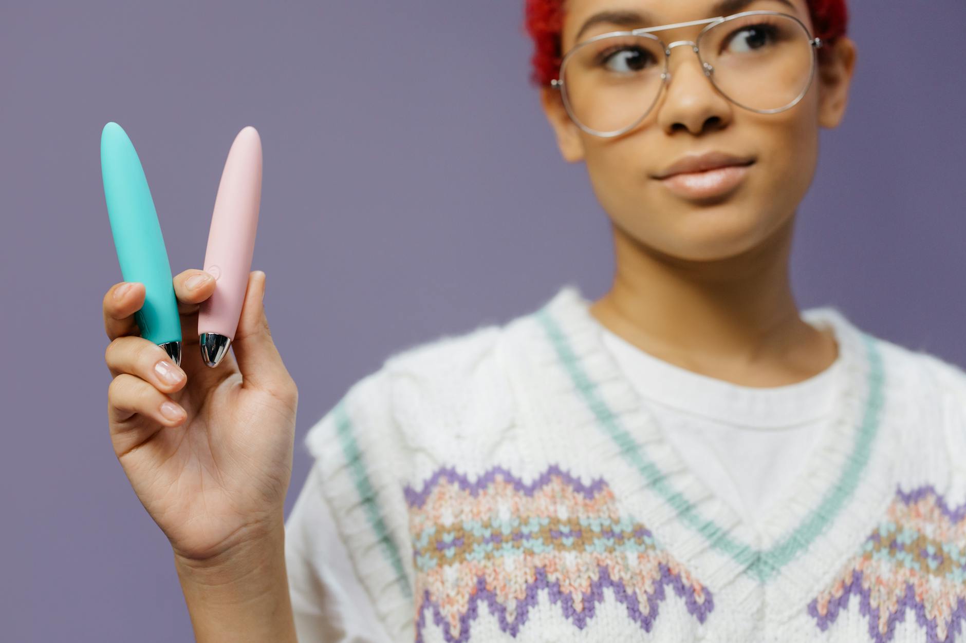 Woman with eyeglasses holding blue and pink silicone vibrators in a contemplative manner