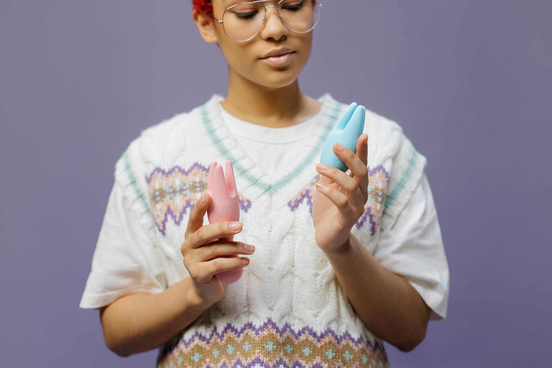 Mujer con gafas sosteniendo vibradores de silicona rosa y azul de manera contemplativa