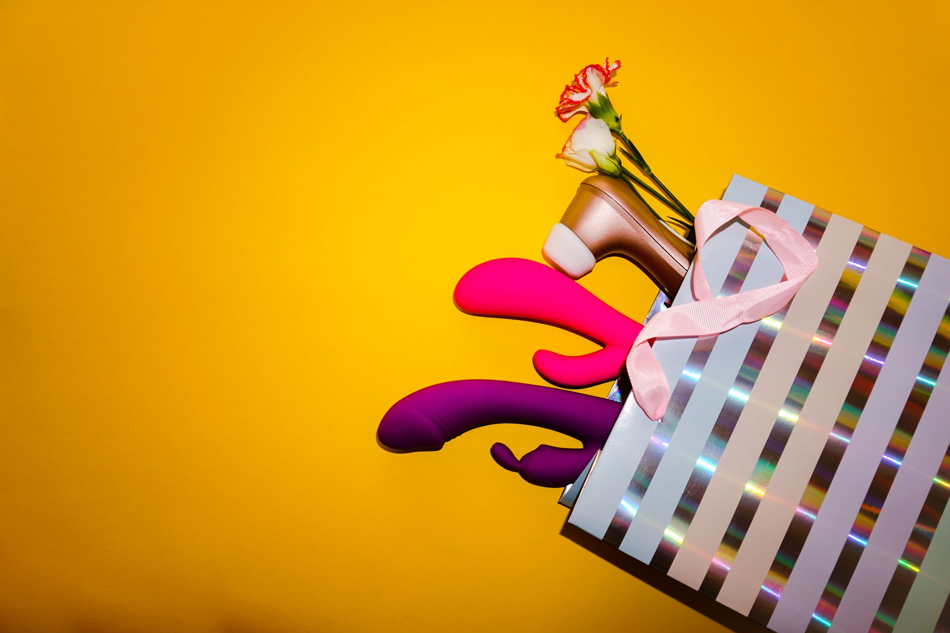 A woman thoughtfully holding a pink vibrator against a yellow background, representing pleasure and choice after relationship transition.