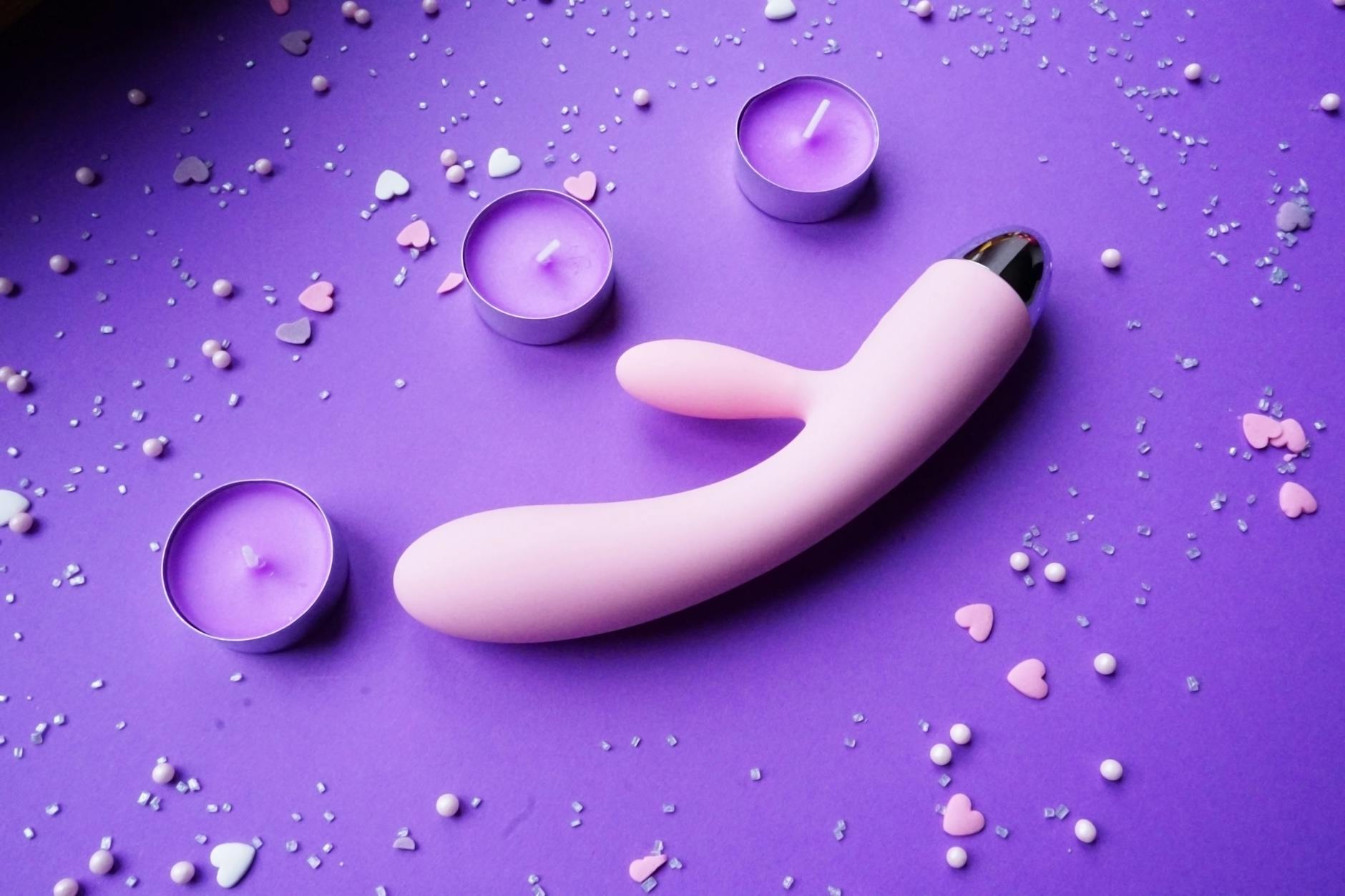 Vibrador rosado sobre fondo púrpura con confeti en forma de corazones y velas para ambiente romántico